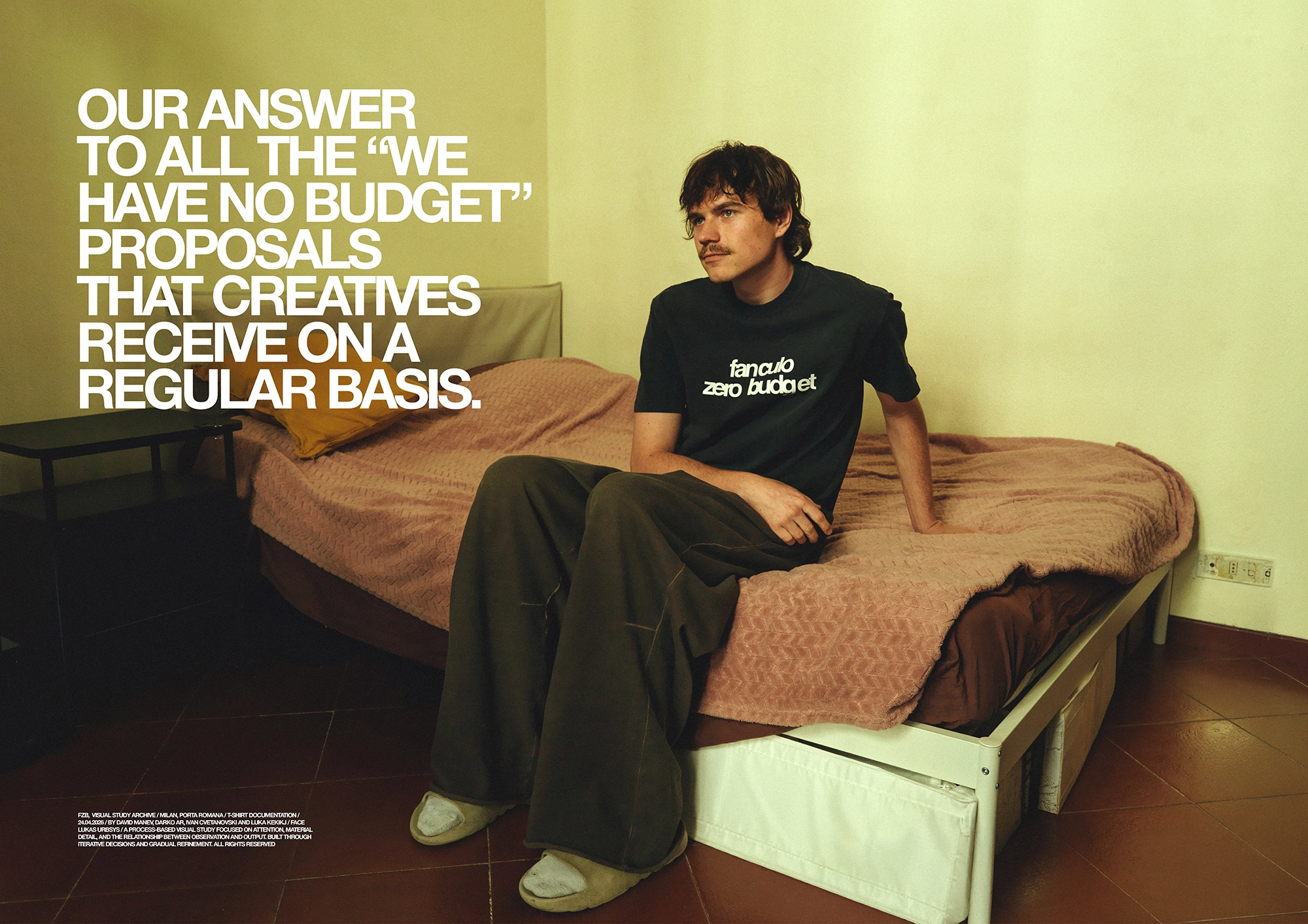 Campaign image showing a person seated on a bed wearing a black T-shirt and wide-leg trousers, with large white typography reading 